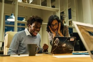 Excited colleagues celebrate a success on a laptop screen in a vibrant office setting.
