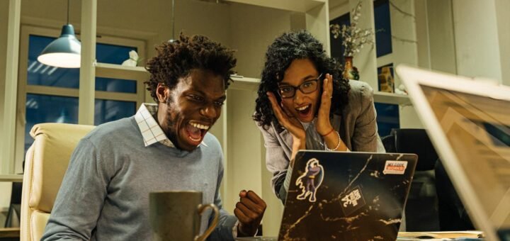 Excited colleagues celebrate a success on a laptop screen in a vibrant office setting.