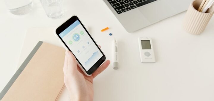 A person checks glucose levels on a smartphone app next to diabetes monitoring equipment.