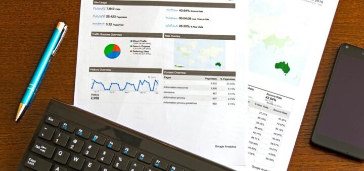 Flatlay of a business analytics report, keyboard, pen, and smartphone on a wooden desk.