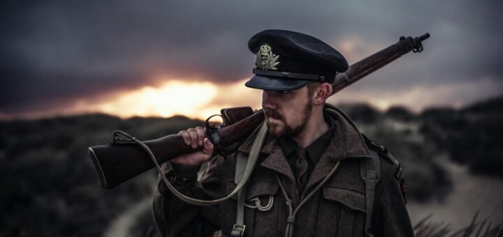 A soldier in uniform holding a rifle against a dramatic sunset background.
