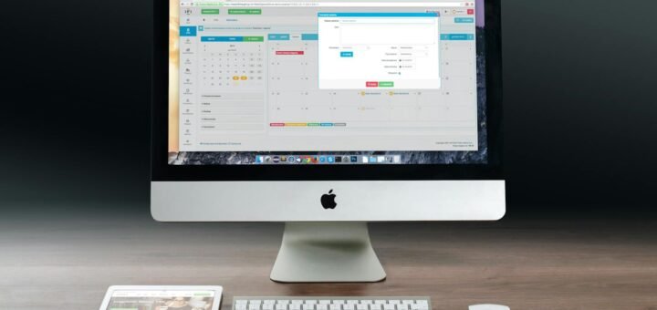 A sleek office setup featuring an Apple iMac, iPad, and keyboard on a wooden desk.