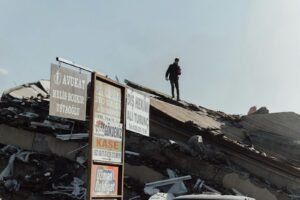 A man walks over debris in a demolished urban area with visible signs.
