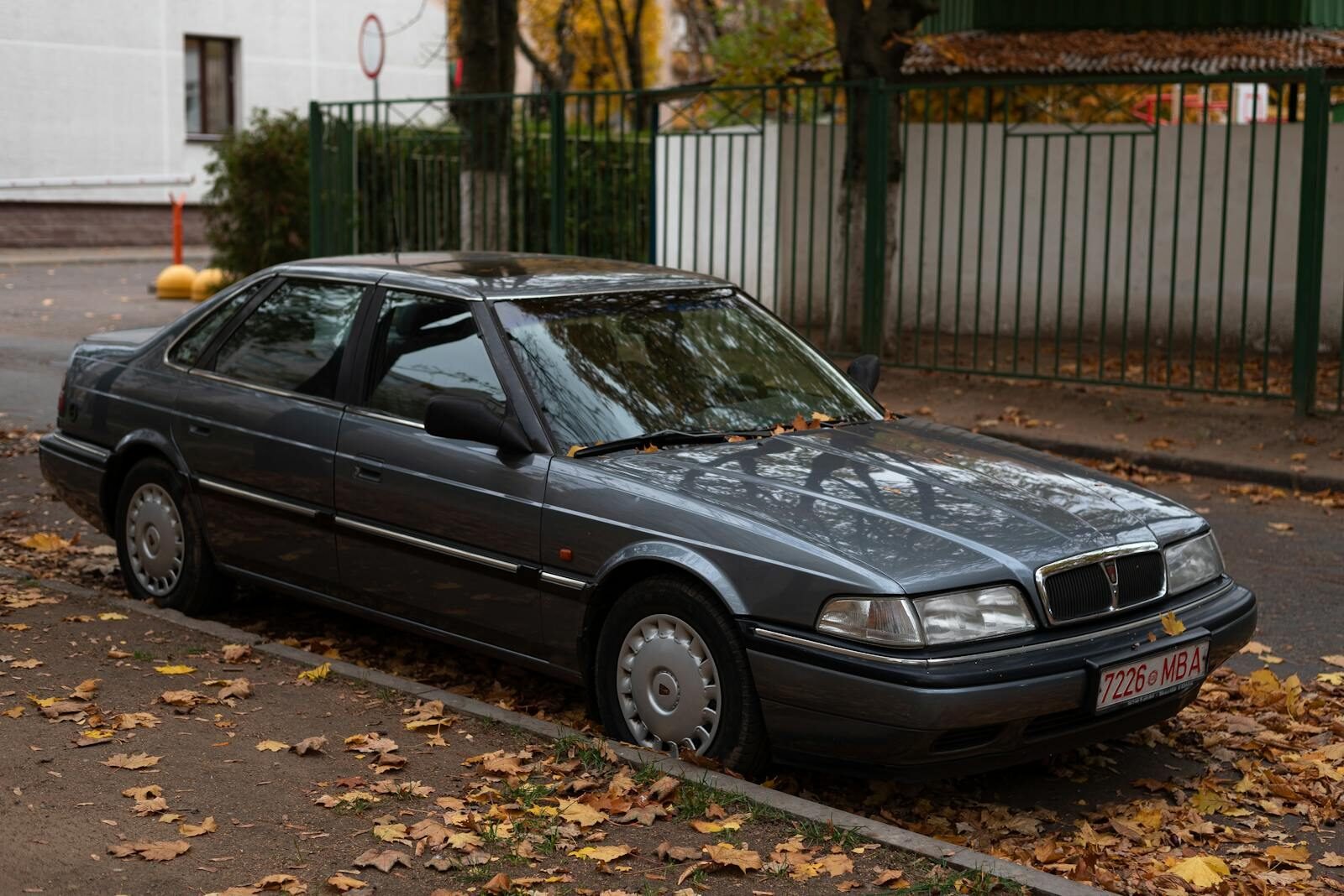 Vintage car parked on a leaf-strewn street in autumn, showcasing urban scenery.