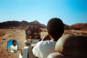Off-road jeep driving through arid desert landscape under clear blue sky.