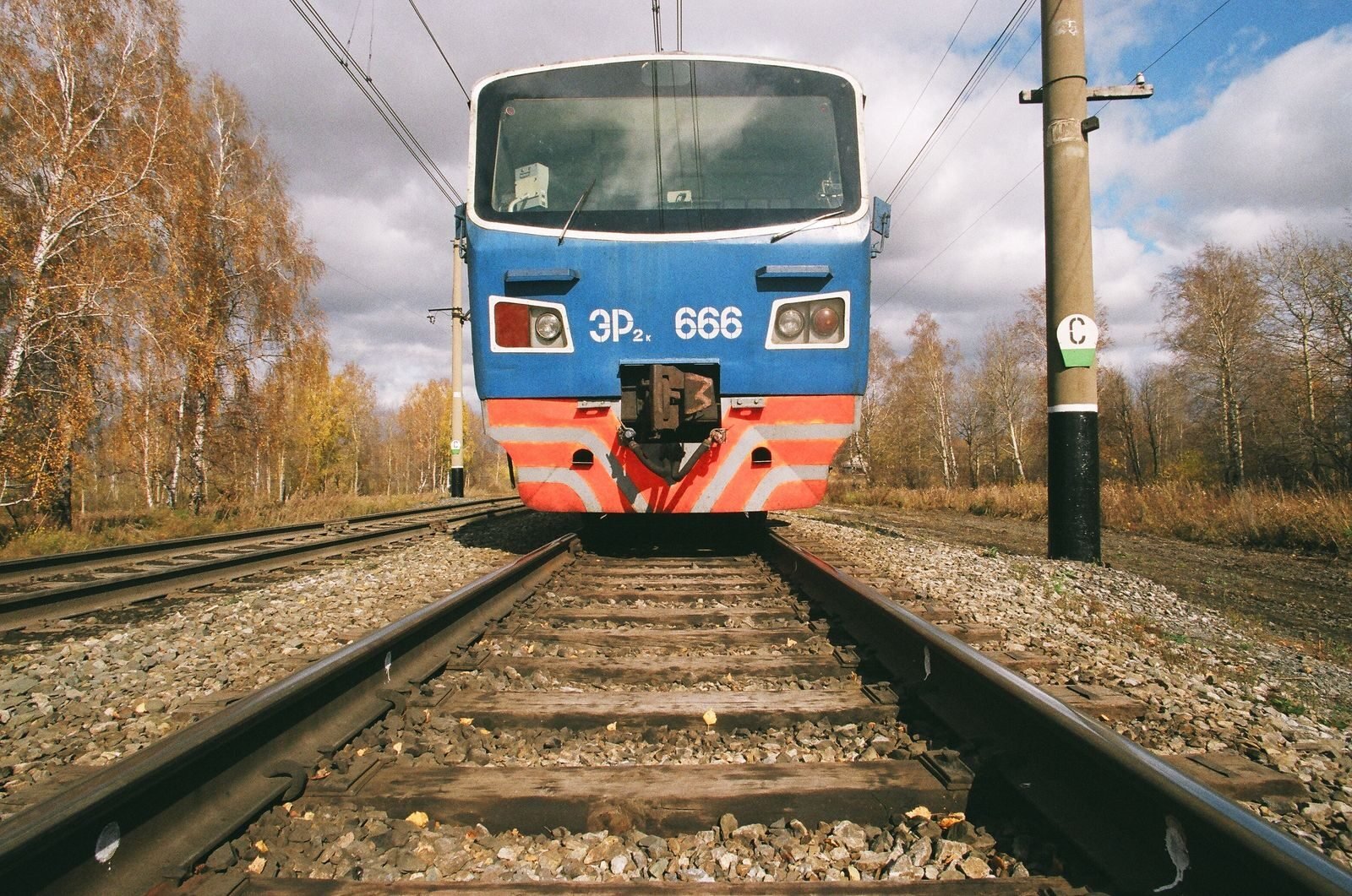 Front view of a blue train on railway tracks, surrounded by trees in autumn.
