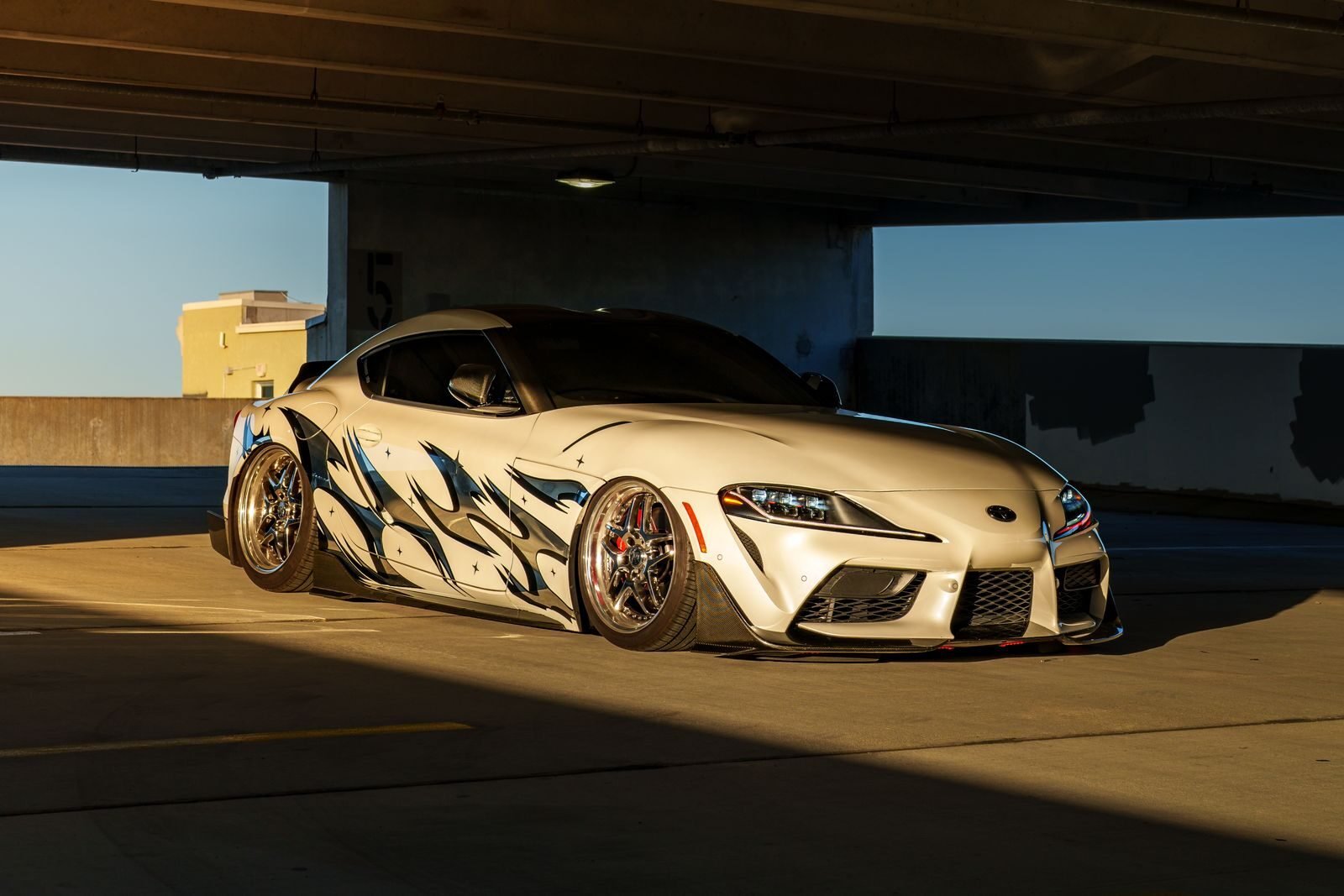 Custom sports car with artistic decals in a sunlit urban parking garage.