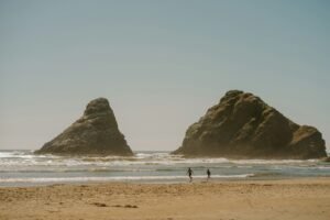 Two people walking on a beach near large sea stacks.