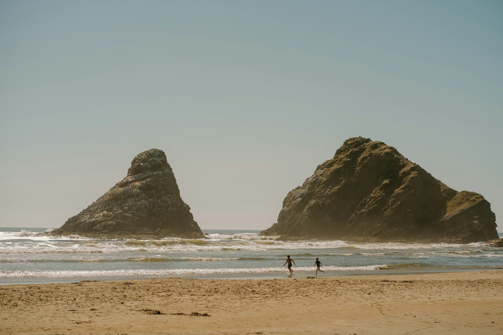 Two people walking on a beach near large sea stacks.