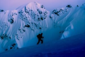 A lone climber ascends a snowy mountain at twilight