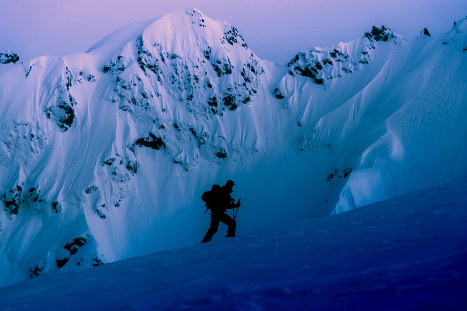 A lone climber ascends a snowy mountain at twilight