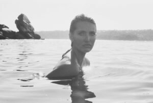 A woman in the water with a rocky outcrop in the background, black and white